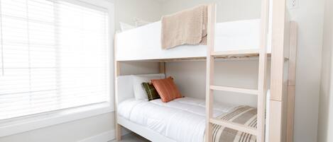 A bunk bed with a ladder, white bedding, and a window with blinds.