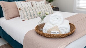 A neatly made bed with a teal headboard, a woven basket containing rolled towels, and a label that reads "SOAP." - Sleeps 8! New Condo Near Downtown Waterfront (Sandusky)
