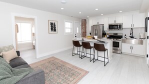 A modern kitchen with white cabinets, stainless steel appliances, and a central island with bar stools. - Sleeps 8! New Condo Near Downtown Waterfront (Sandusky)