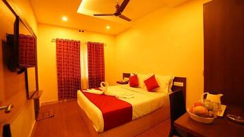 Quarto de hotel com uma cama, uma escrivaninha com uma cesta de frutas e um ventilador de teto.