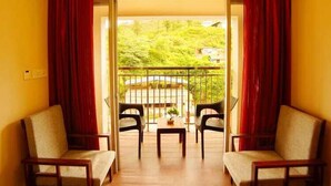 A room with a wooden floor, two chairs, a small table, and a view of greenery through a glass door.