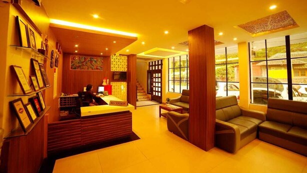 A hotel lobby with a reception desk, seating area, and large windows offering a view of the outside.