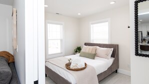 Un dormitorio con cama, mesita de noche, espejo y ventana.
