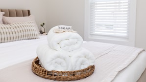 A neatly made bed with a white comforter and a basket of folded towels on a woven tray. - Sleeps 6! Modern & Upgraded Boutique Condo (Sandusky)