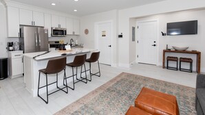 A modern kitchen with white cabinets, a stainless steel refrigerator, a microwave, and a large island with bar stools. - Sleeps 6! Modern & Upgraded Boutique Condo (Sandusky)