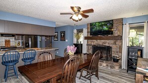 A dining area with a wooden table and chairs, a fireplace, and a television mounted on the wall. - 01105 - 5 Montserrat Lane (Hot Springs)
