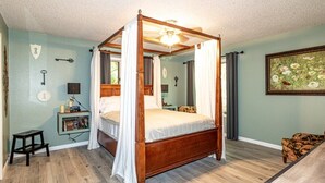 A four-poster canopy bed with a ceiling fan, a bedside table with books, and a small stool. - 01105 - 5 Montserrat Lane (Hot Springs)
