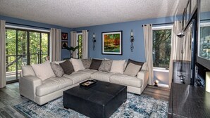A modern living room with a sectional sofa, a coffee table, and a large window with curtains. - 01105 - 5 Montserrat Lane (Hot Springs)