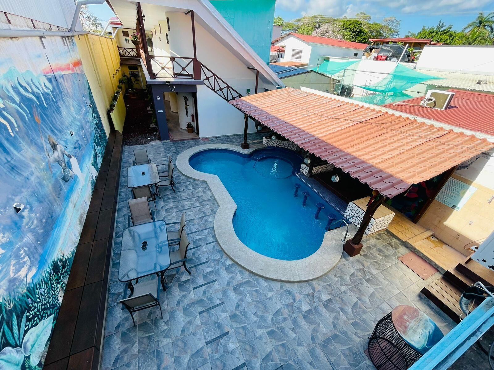 Una piscina en la azotea con forma original, rodeada de mobiliario exterior y un mural.