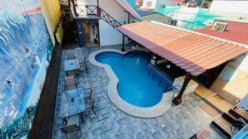 Una piscina en la azotea con forma original, rodeada de mobiliario exterior y un mural.