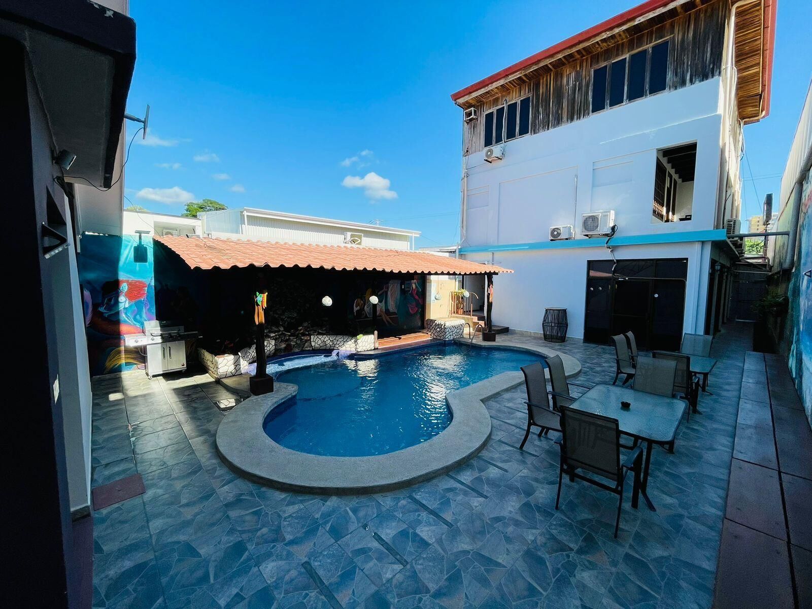 Piscina com deck revestido em pedra, cercada por área de estar externa e espaço coberto com telhado em azulejo.