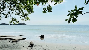 A beach with calm water, scattered rocks, and a distant island. - Poseidon Party Hotel In Downtown (Jacó)