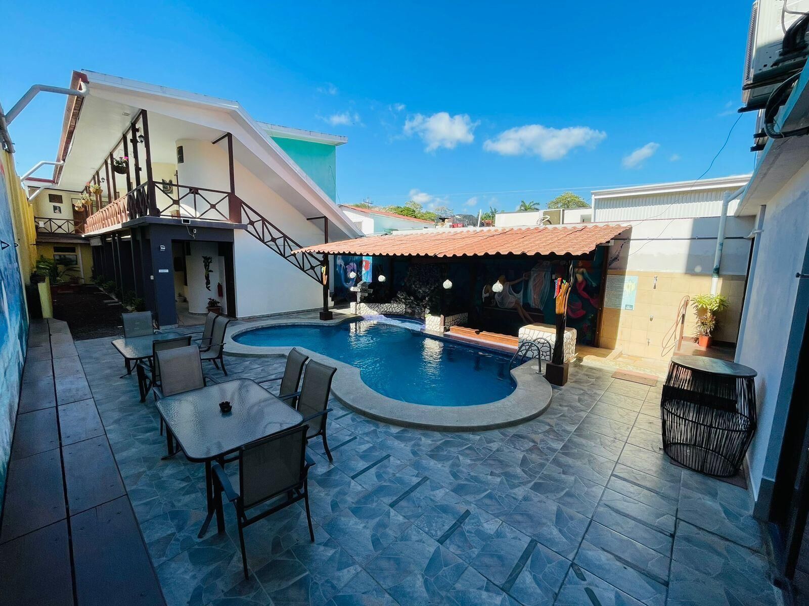 Une piscine avec une terrasse carrelée, des sièges extérieurs et un espace couvert doté d’un toit rouge.