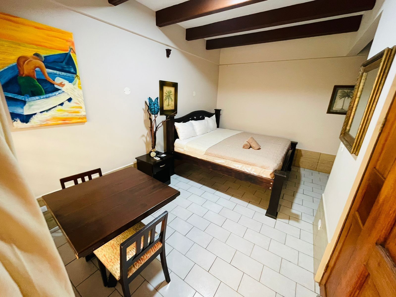 Une chambre à coucher avec un lit, une table de chevet, une chaise, un tableau accroché au mur et une poutre en bois au plafond.