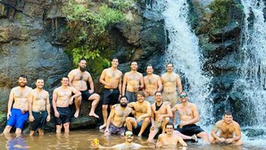 A group of people in a natural setting with a waterfall and rocky terrain. - Poseidon Party Hotel In Downtown (Jacó)