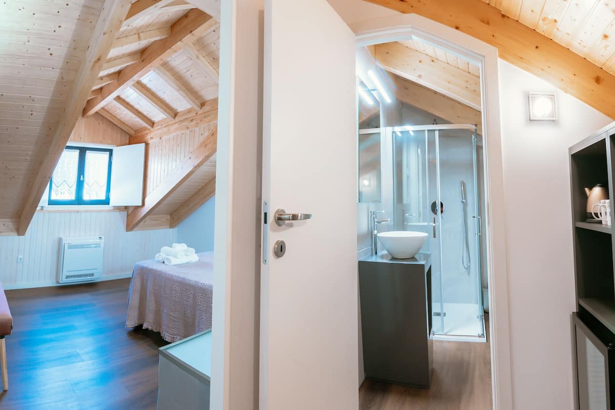 Une chambre moderne et compacte, dotée d’un plafond en pente, d’un petit coin salon et d’une salle de bain avec une paroi en verre.
