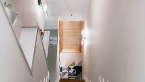 Un escalier avec des marches en bois et des rampes blanches, menant à une pièce dotée d’une porte en bois et d’un motif géométrique sur le mur.