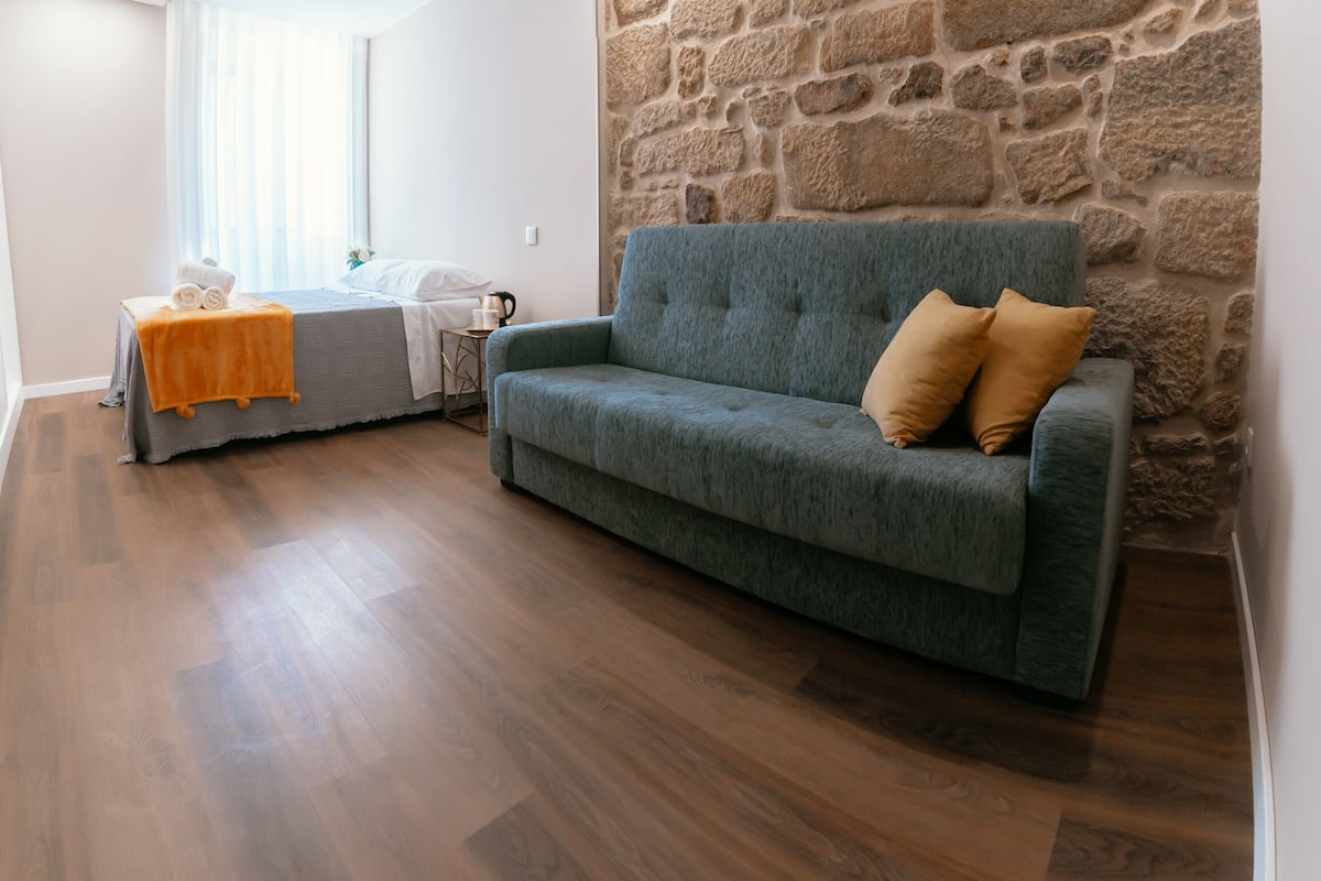 Une pièce avec un canapé gris, une petite table recouverte d’une nappe jaune et un mur en pierre.