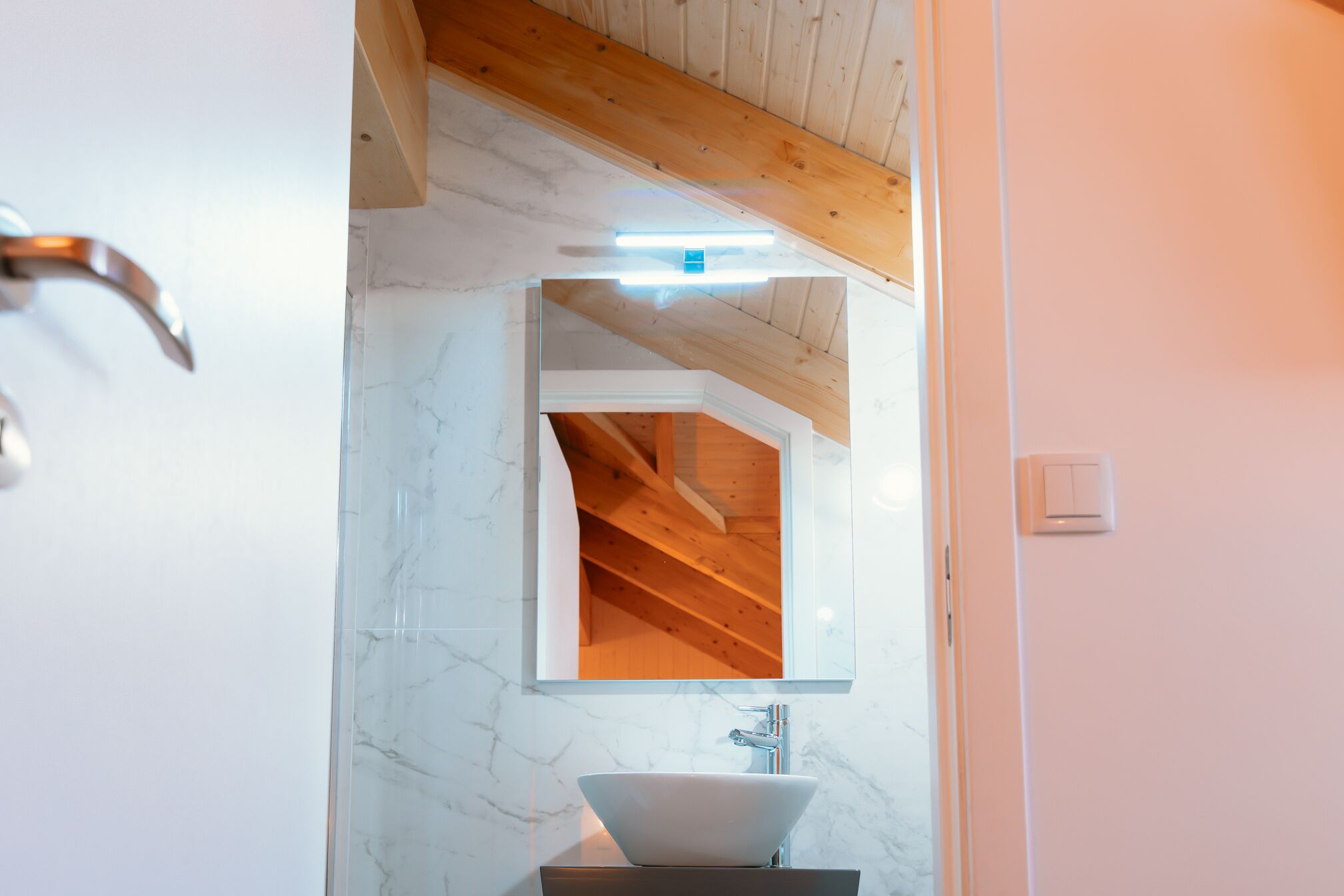 Un baño con lavamanos de mármol blanco, vigas de madera en el techo y un espejo.