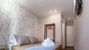 Un dormitorio con cama, almohadas, mesita de noche y un perchero en la pared.
