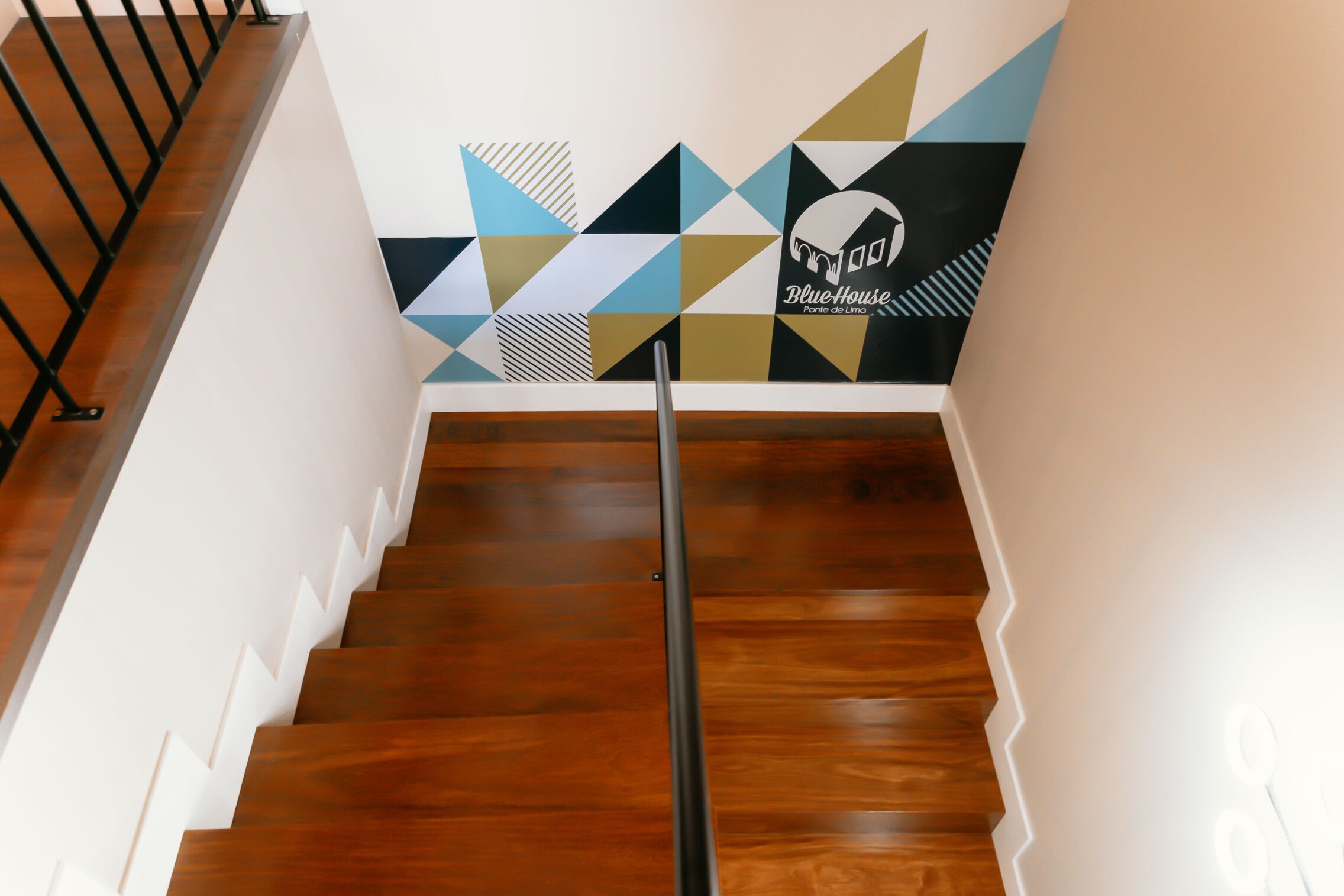 A wooden staircase with a geometric wall mural and a metal handrail.