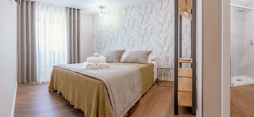 A hotel room with a bed, a wooden side table, a mirror, and a shower area.