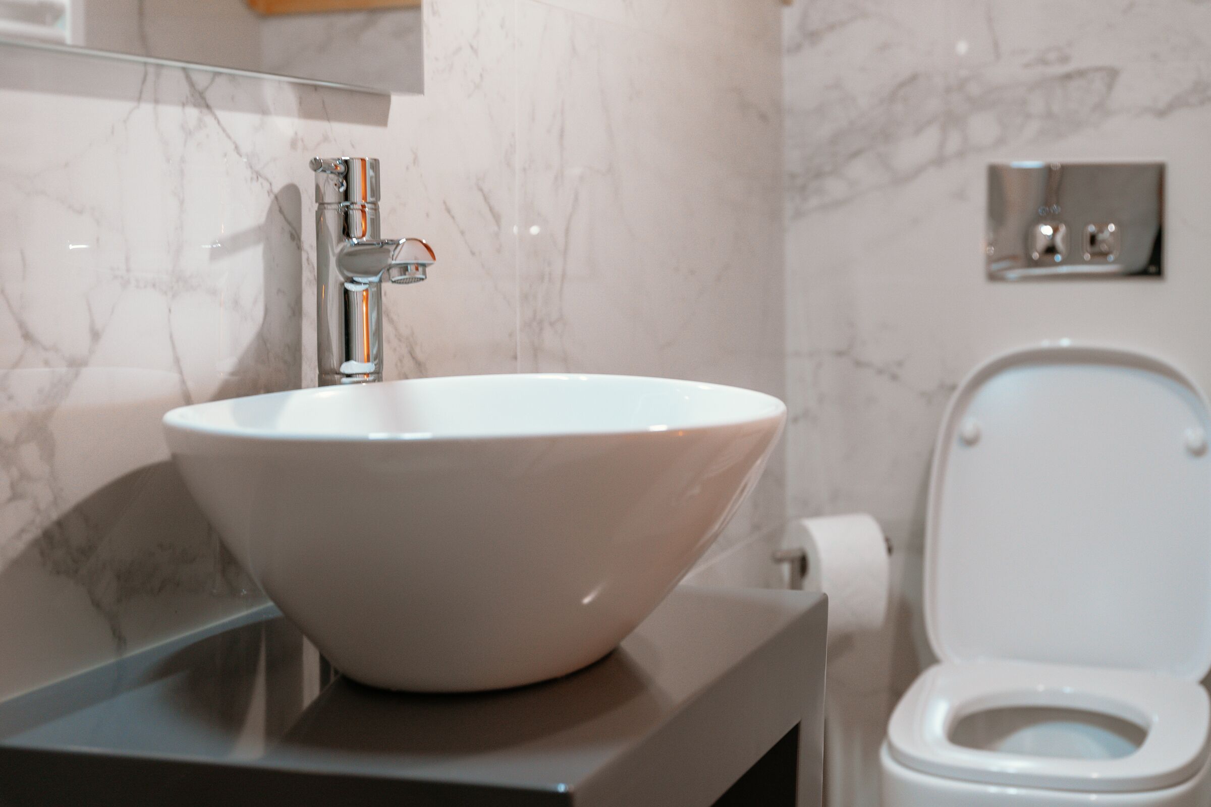 A bathroom with a white marble sink, a modern faucet, and a toilet.