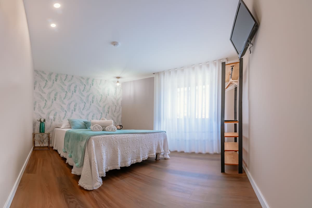 Une chambre à coucher avec un lit, une télévision, une armoire et une fenêtre avec des rideaux.