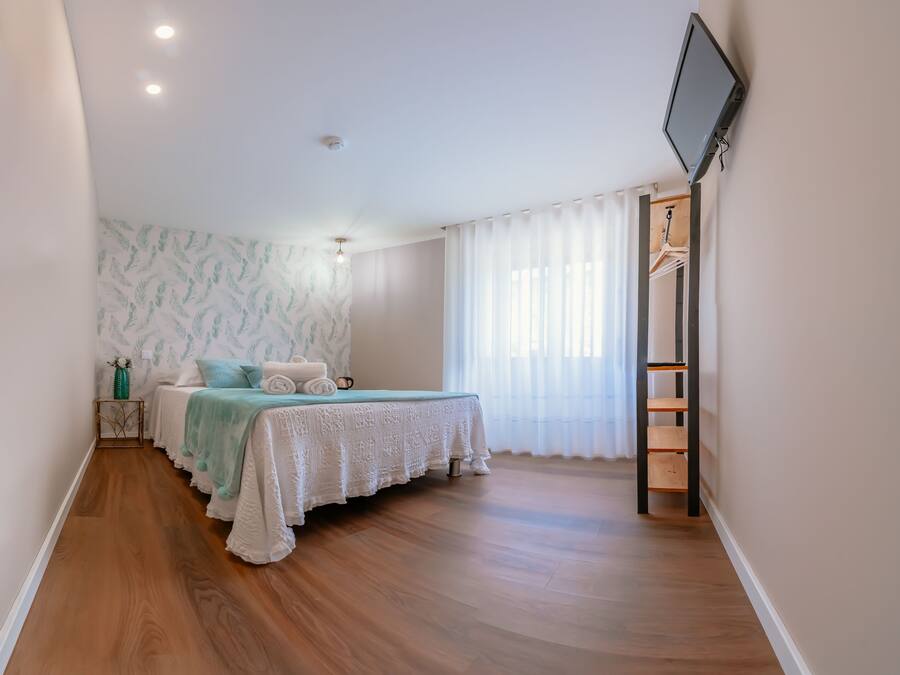 A bedroom with a bed, a TV, a wardrobe, and a window with curtains.