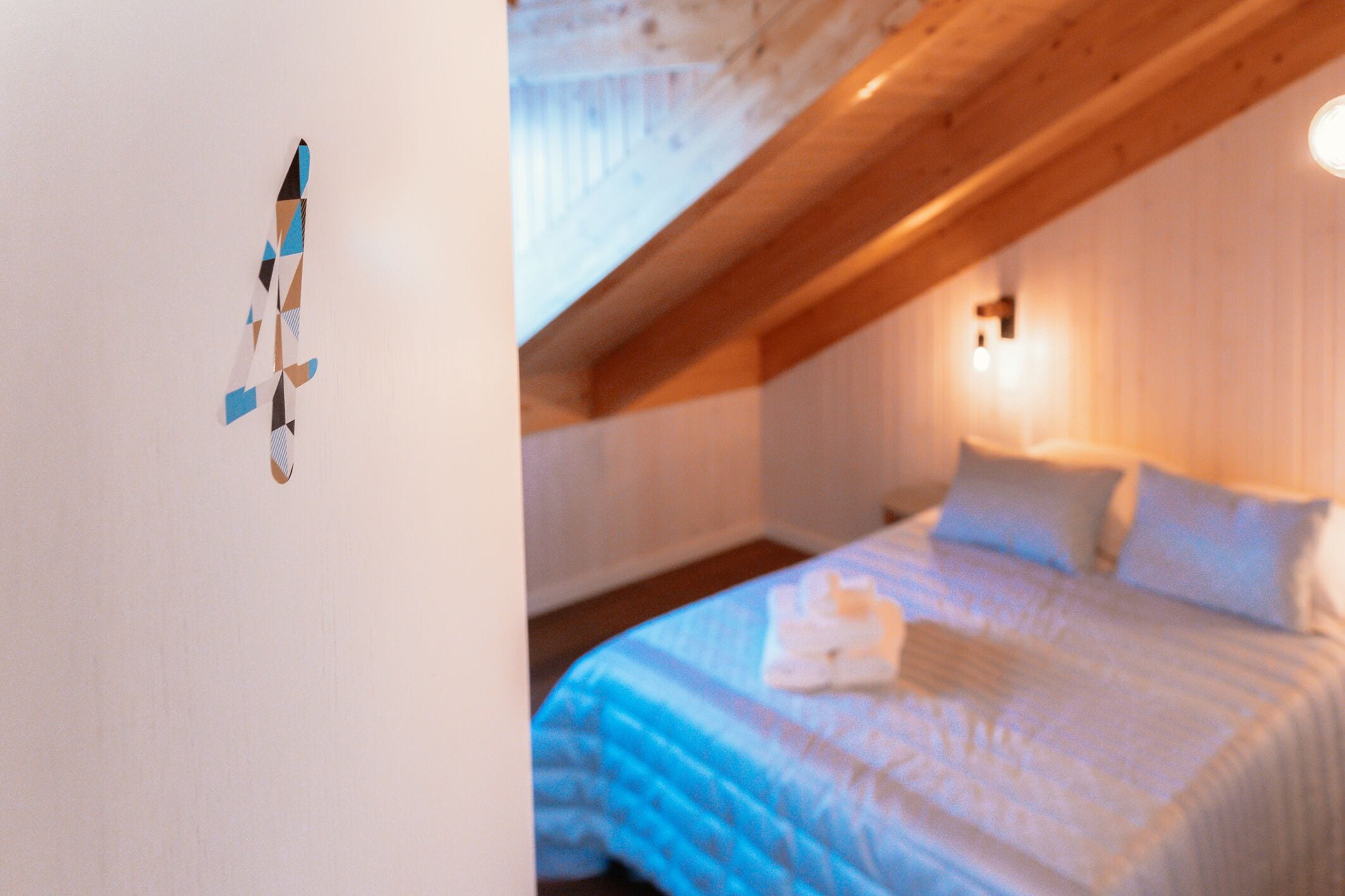 A bedroom with a sloped ceiling, a bed with white bedding, and a wall-mounted light fixture.