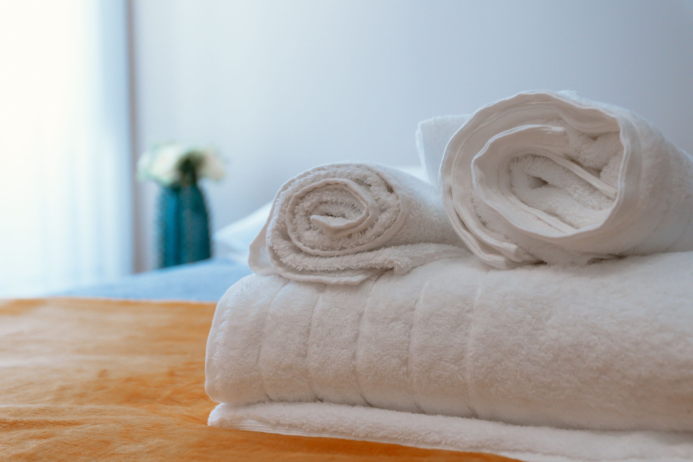 A neatly folded white towel on a bed with an orange headboard.