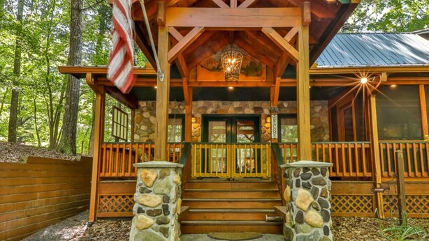 Uma cabana de madeira com entrada de pedra, um alpendre com grade e uma placa de boas-vindas.