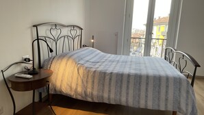 A bedroom with a bed, a bedside table, a lamp, and a window with a view of buildings. - Casa di Silvia Appartamento a soli 20 Minuti a piedi dal suggestivo Lago di Como (Como)