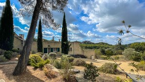 Una villa de estilo mediterráneo con fachada de piedra, un jardín de cipreses y vistas a las colinas circundantes.