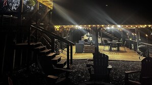 A covered outdoor seating area with a table and chairs, a barbecue grill, and a staircase leading to an upper level.