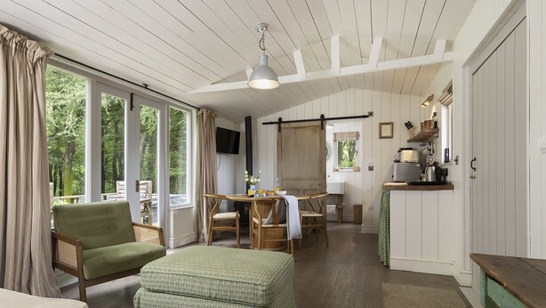 A room with a bed, a dining table with chairs, a kitchen area, and large windows. - Two dog friendly holiday properties with hot tub - Keepers Homes (Cranham)