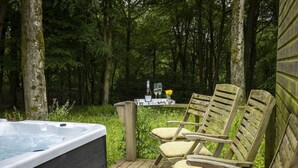 A wooden deck with a hot tub, two wooden chairs, and a table with a bottle and glasses. - Two dog friendly holiday properties with hot tub - Keepers Homes (Cranham)