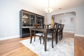A dining area with a wooden table and chairs, a chandelier, and a large cabinet with glass doors. - Your home away from home awaits. Cozy 4-bedroom house with tons of space for all (San Antonio)