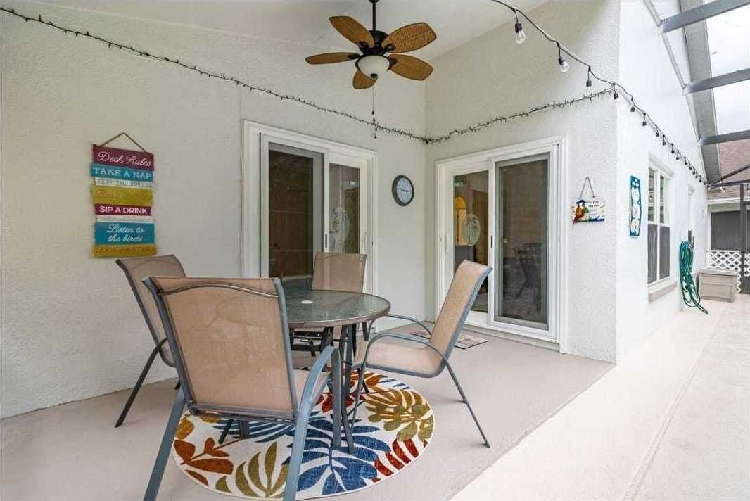 A covered patio area with a round table and chairs, a ceiling fan, and string lights.
