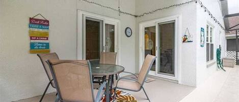 A covered patio area with a round table and chairs, a ceiling fan, and string lights.
