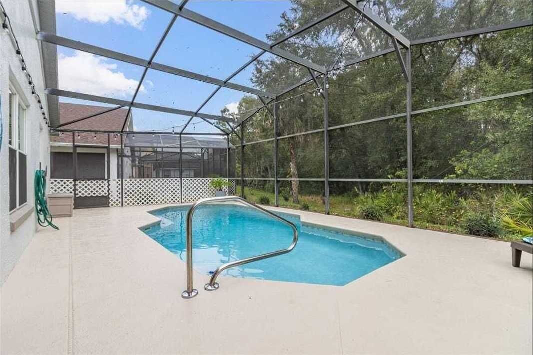 An indoor swimming pool with a metal pool ladder, surrounded by a covered area with a metal fence and trees in the background.