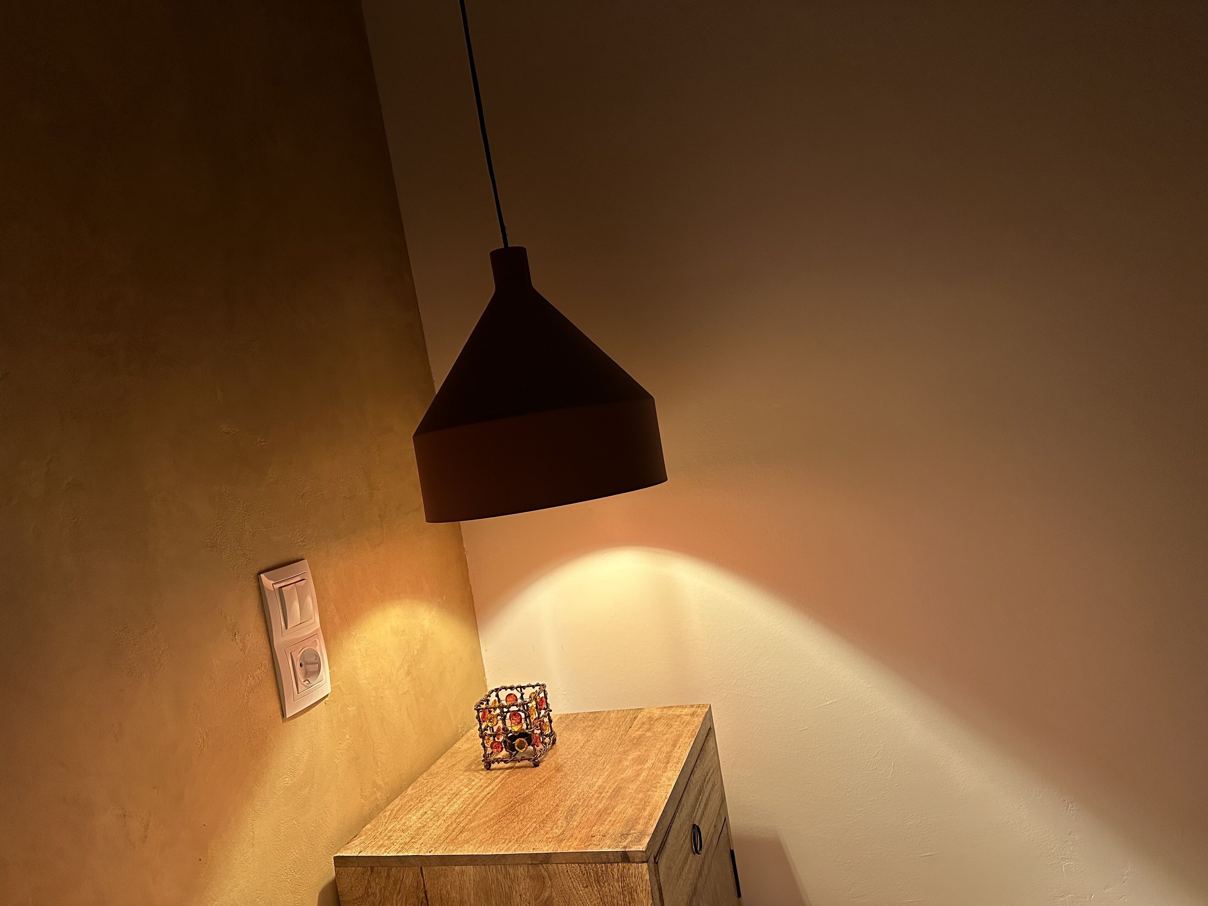 Un mueble de madera con un adorno encima, una lámpara de pared y un interruptor.