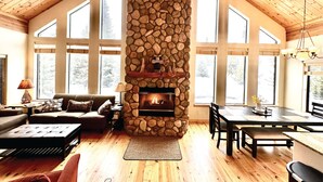 A spacious living room with a stone fireplace, wooden ceiling, and large windows. - Cozy Cabin Escape: Nature, Comfort, and Serenity Await! (Grand Lake)
