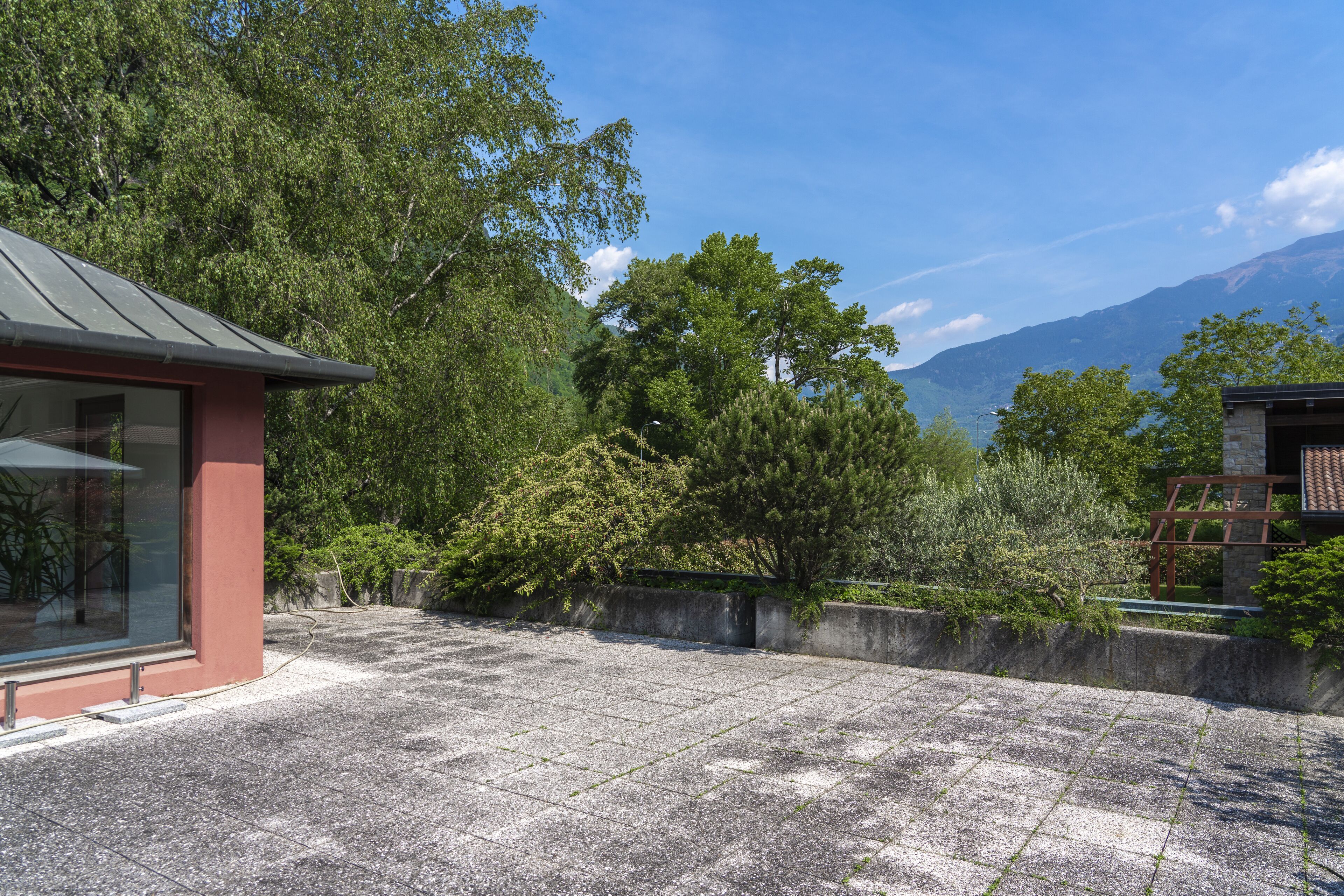 A courtyard with a stone floor, a glass building with a red exterior, and a view of mountains.