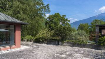 A courtyard with a stone floor, a glass building with a red exterior, and a view of mountains.
