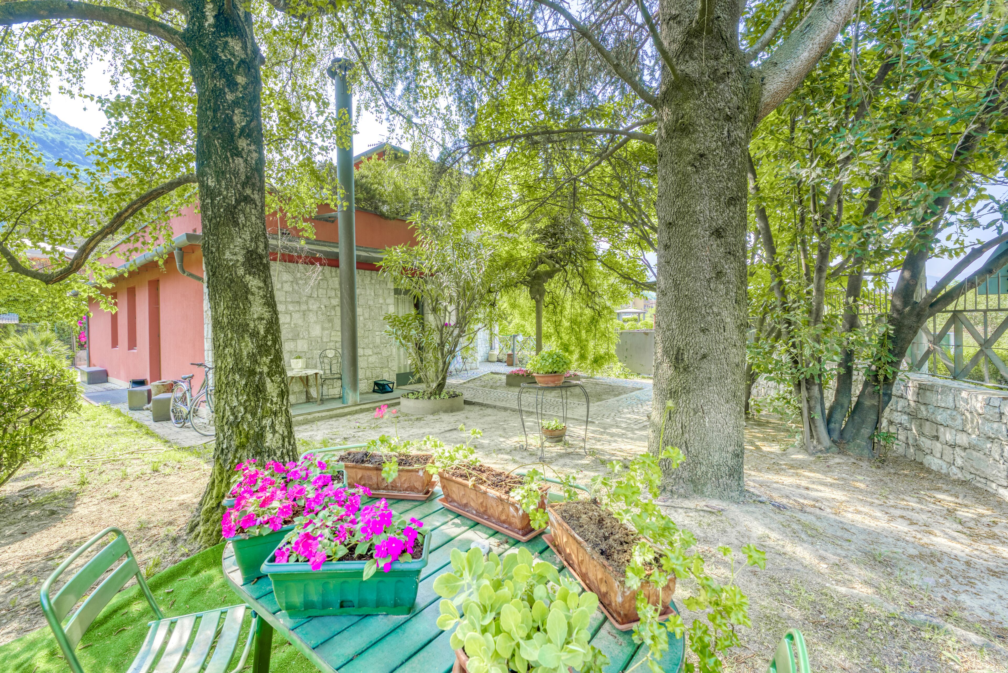 Ein Gartenbereich mit Holz-Pflanzkästen, Blumen und Pflanzen, einer grünen Bank und einem Steinhaus im Hintergrund.