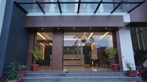 Entrada de un edificio moderno con puertas de cristal, plantas en macetas y un mostrador de recepción visible en el interior.
