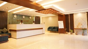 Zona de recepción de un hotel con mostrador, asientos y una pared con nombres de ciudades.