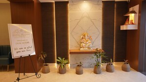 Zona de recepción de hotel con un cartel de bienvenida, una estatua y plantas en macetas.