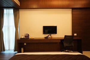 Habitación de hotel con cama, escritorio con televisor de pantalla plana, silla y un pequeño cubo de basura.